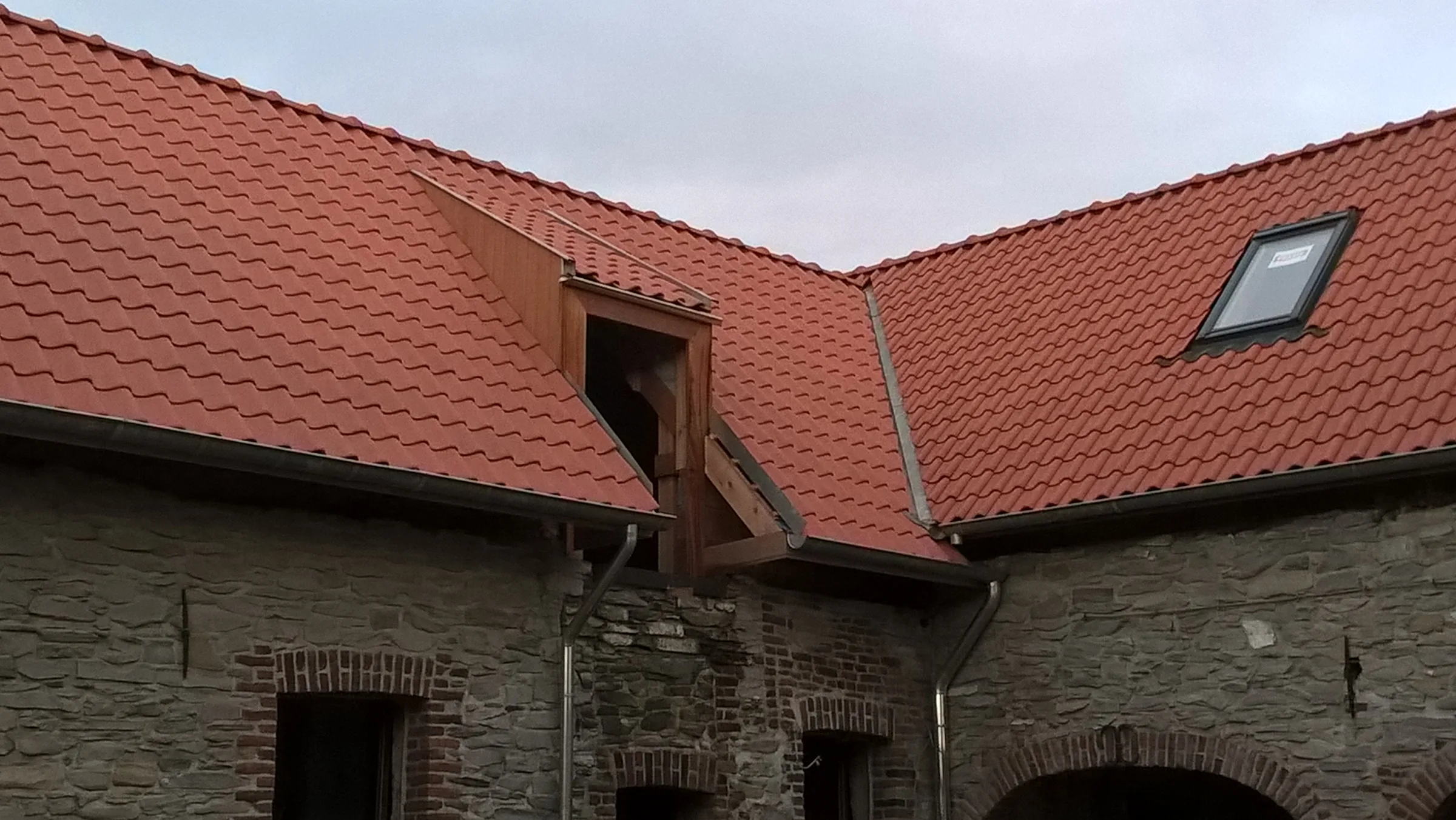 Couverture en tuiles rouges avec lucarne en bois et fenêtre de toit sur un bâtiment en pierre